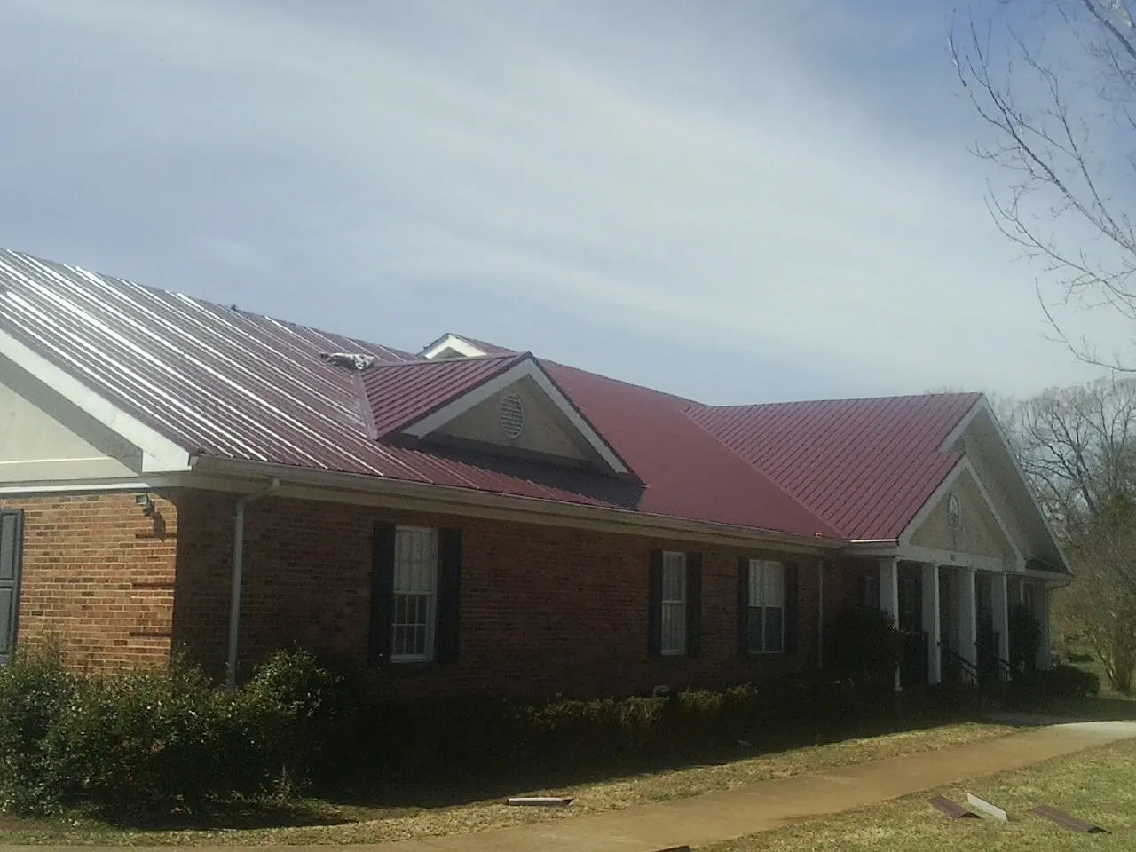 Red metal roof with gabled entries on a long brick building, from a Hail Damage Roof Repair job in Clayton
